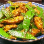 Chicken and Snow Peas Stir Fry featuring juicy chicken strips and crisp snow peas coated in savory sauce on a patterned blue bowl.