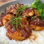 Glazed Soy Garlic Chicken Thighs served with steamed white rice and broccoli, topped with sesame seeds and sliced green onions.