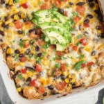 Southwest Chicken Casserole topped with melted cheese, black beans, corn, tomatoes, and sliced avocado in a white baking dish.