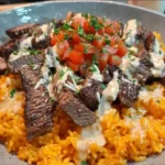 Steak Queso Rice with juicy steak strips, creamy queso sauce, and vibrant diced tomatoes over flavorful rice