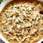 Shredded Crock Pot Chicken and Gravy in a white bowl, garnished with chopped parsley.
