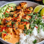 Coconut Chicken Rice Bowl topped with grilled chicken, creamy coconut sauce, avocado slices, cilantro, and lime wedges.