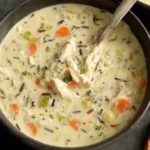 Creamy Copycat Panera Chicken and Wild Rice Soup with carrots, celery, and shredded chicken in a black bowl