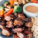 Hibachi Steak with brown rice, dipping sauce, and stir-fried vegetables on a blue plate.