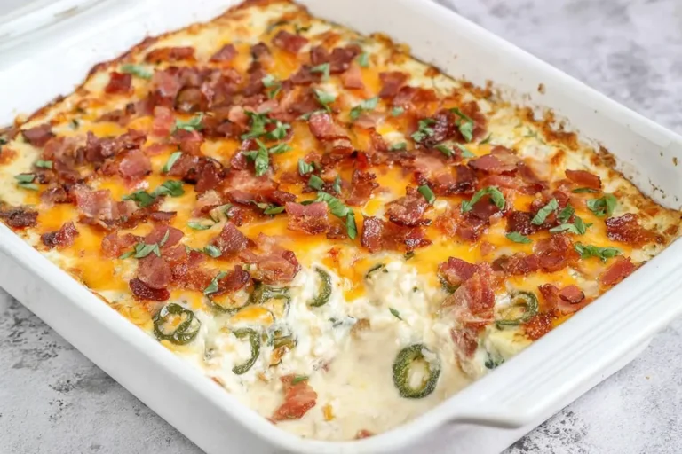 Keto Jalapeno Popper Casserole topped with crispy bacon, cheddar cheese, and fresh herbs in a white baking dish.