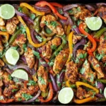 Sheet Pan Chicken Fajitas with spiced chicken pieces, colorful bell peppers, red onions, lime slices, and fresh cilantro on a baking sheet