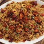 Spicy BBQ Chicken Fried Rice with a Japanese BBQ twist, garnished with cashews, red chili slices, and herbs on a white platter.