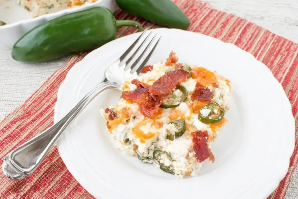 A serving of Keto Jalapeno Popper Casserole with bacon, jalapeños, and cheese on a white plate with a fork.