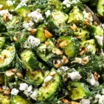 Close-up of smashed cucumber salad with fresh dill, feta, and chopped pistachios.