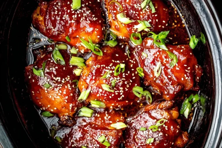 Crock Pot Honey Garlic Chicken thighs in a slow cooker, glazed with sweet garlic sauce, garnished with sesame seeds and green onions.