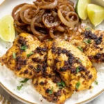 Grilled Cuban chicken breasts with sautéed onions and lime wedges served over white rice in a bowl.