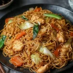 Plated chicken chow mein with stir-fried noodles, vegetables, and tender chicken pieces.