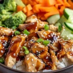 Teriyaki Chicken Rice Bowl with glazed chicken pieces, white rice, broccoli, cucumbers, and carrots topped with sesame seeds and green onions.
