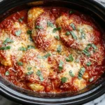 Crockpot Chicken Parmesan topped with melted cheese, marinara sauce, and fresh basil in a slow cooker.