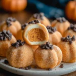 Pumpkin Cheesecake Truffles coated in sugar and topped with chocolate chips, shaped like mini pumpkins on a plate.