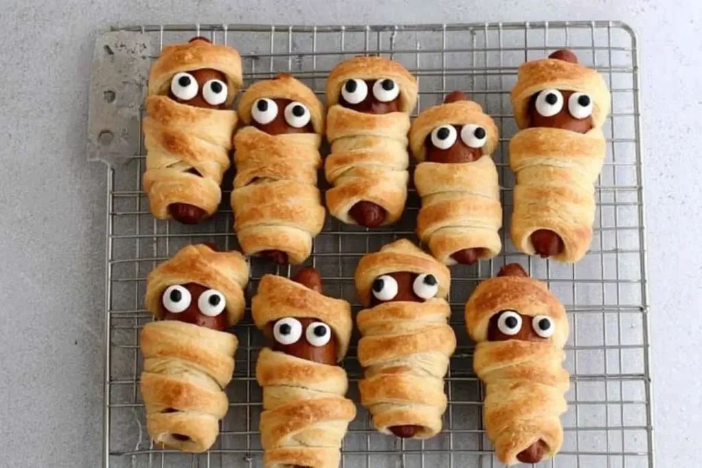 Mummy Pigs in a Blanket hot dogs wrapped in crescent rolls with candy eyes, a spooky and fun Halloween snack.