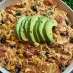 A bowl of creamy Slow Cooker Fiesta Chicken made with shredded chicken, corn, black beans, tomatoes, and topped with fresh avocado slices.
