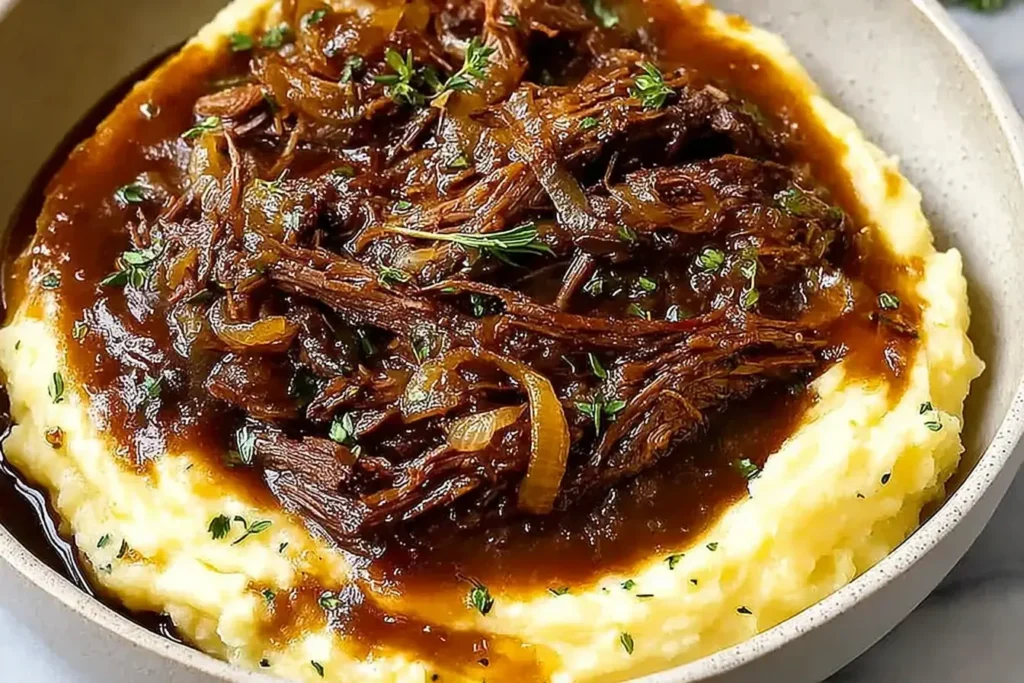 Plated French Onion Pot Roast served over creamy mashed potatoes, topped with caramelized onions and rich onion gravy.
