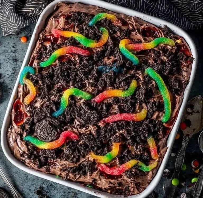 Colorful gummy worms on top of a rich chocolate pudding dirt cake layered with crushed Oreos and creamy frosting in a white baking dish.