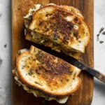 Caramelized Onion and Apple Grilled Cheese Sandwich on a wooden board, sliced in half and perfectly toasted with melted cheese oozing out.