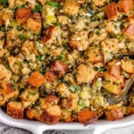 Golden-brown traditional Thanksgiving stuffing baked with herbs, celery, and toasted bread cubes in a white casserole dish.
