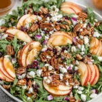 Fresh Apple Arugula Salad with sliced apples, goat cheese, maple pecans, and balsamic dressing served on a white plate.