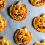 Golden-brown spooky chorizo hand pies shaped like jack-o’-lanterns on a baking sheet, perfect for a festive Halloween treat.