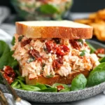 Creamy Sun Dried Tomato Chicken Salad sandwich on fresh bread with spinach leaves and chips on the side.