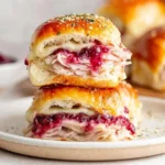 Havarti Cranberry Turkey Sliders stacked on a plate with melted cheese, tender turkey, and sweet cranberry sauce on golden Hawaiian rolls.
