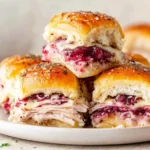 Havarti Cranberry Turkey Sliders stacked on a plate, layered with sliced turkey, melted Havarti cheese, and cranberry sauce on golden baked rolls.