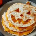 Jack O Lantern Quesadillas filled with melted cheddar cheese on a plate, perfect festive Halloween snack.