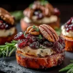 Sweet Potato Rounds with Brie Cranberry and Pecans topped with toasted nuts and fresh herbs on a dark slate serving board