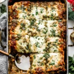 Golden-baked Christmas Eve Lasagna topped with melted cheese, pesto, and fresh herbs in a festive holiday setting.