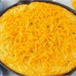 Golden-baked Paula Deen’s Corn Casserole topped with melted cheddar cheese in a cast iron skillet.