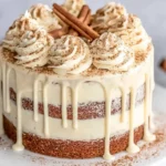 Christmas Spice Cake with Eggnog Buttercream topped with cinnamon swirls and creamy drip frosting on a white cake stand.