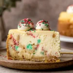 Sugar Cookie Cheesecake slice with Christmas sprinkles and a golden crust.