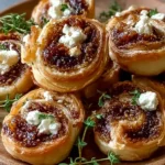 Fig and Goat Cheese Pinwheels stacked on a wooden plate with fresh thyme, showing flaky pastry, rich fig filling, and creamy goat cheese.