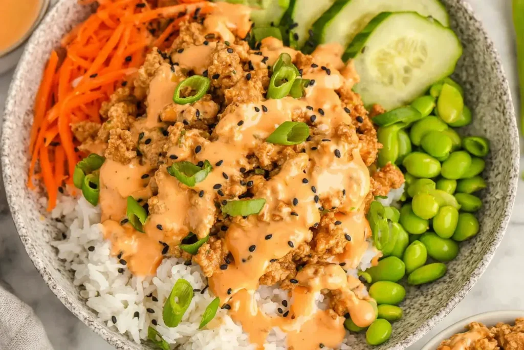 Ground Turkey Rice Bowls topped with creamy bang bang sauce, fresh vegetables, and white rice in a colorful, vibrant bowl.