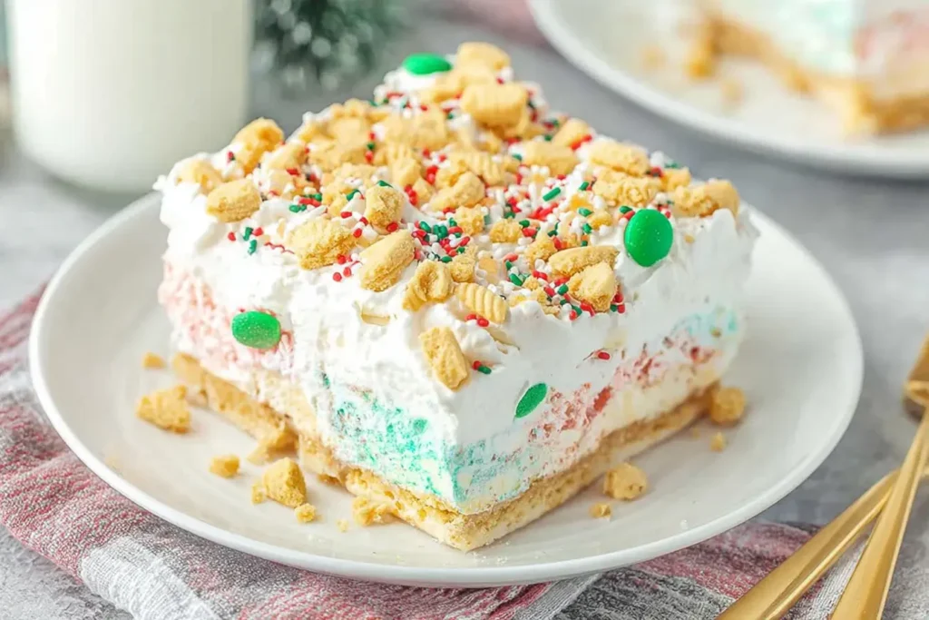 Slice of No Bake Christmas Cookie Lush topped with whipped cream, crushed cookies, and colorful holiday sprinkles on a white plate.