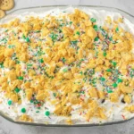 No Bake Christmas Cookie Lush topped with crushed cookies, whipped cream, and festive holiday sprinkles in a glass dish.