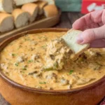 Dipping bread into creamy Slow Cooker Philly Cheesesteak Dip.