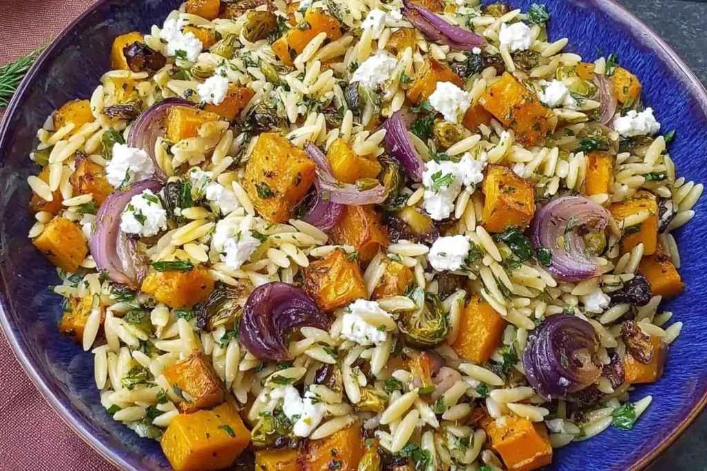 Fall Harvest Orzo Salad with roasted butternut squash, Brussels sprouts, red onions, and goat cheese tossed with orzo in a maple balsamic dressing.