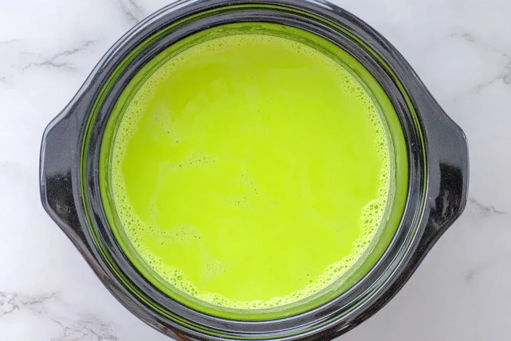 Bright green Grinch Hot Chocolate warming in a black slow cooker for a festive holiday drink.