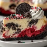 Close-up slice of Christmas Red Velvet Cheesecake topped with Oreos, whipped cream, and festive red and green sprinkles.