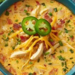Spicy Jalapeño Popper Chicken Soup in a blue bowl topped with cheddar, crispy bacon, and fresh jalapeño slices.