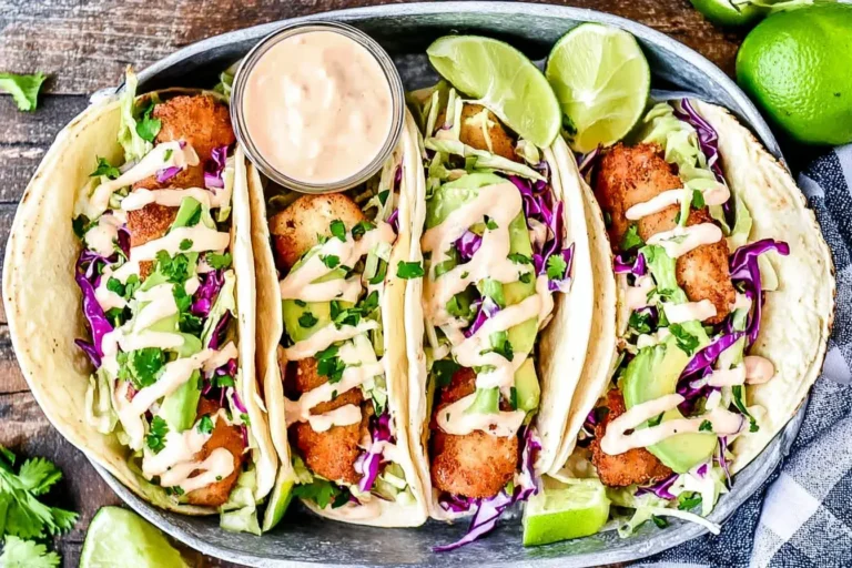 Crispy Baja Fish Tacos with cabbage slaw, avocado, and chipotle mayo drizzle served with lime wedges.