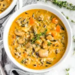 Creamy bowl of Vegan Pumpkin Wild Rice Soup with mushrooms, carrots, and herbs in a white bowl.