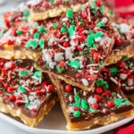 Plate of festive Christmas Crack Recipe pieces topped with red, green, and white sprinkles over chocolate and caramel toffee layers.