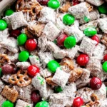 Close-up of Reindeer Food snack mix with powdered sugar–coated Chex, pretzels, and red-green candies in a festive bowl.