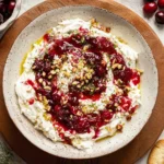 Cranberry Whipped Feta Dip topped with cranberry sauce, chopped pistachios, and honey in a rustic bowl.
